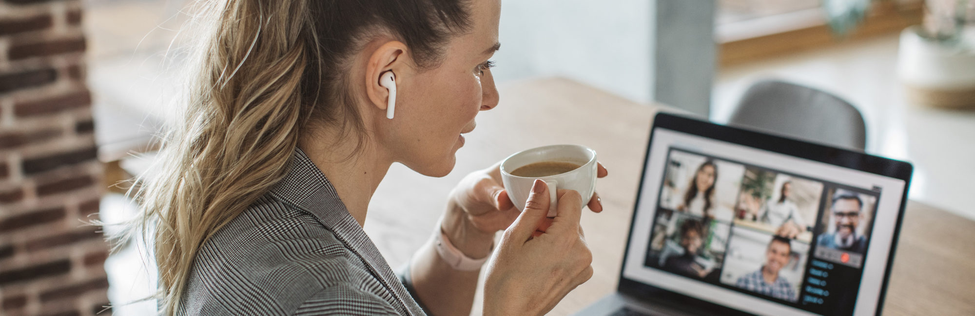 A woman on a conference call on laptop sipping a cup of coffee